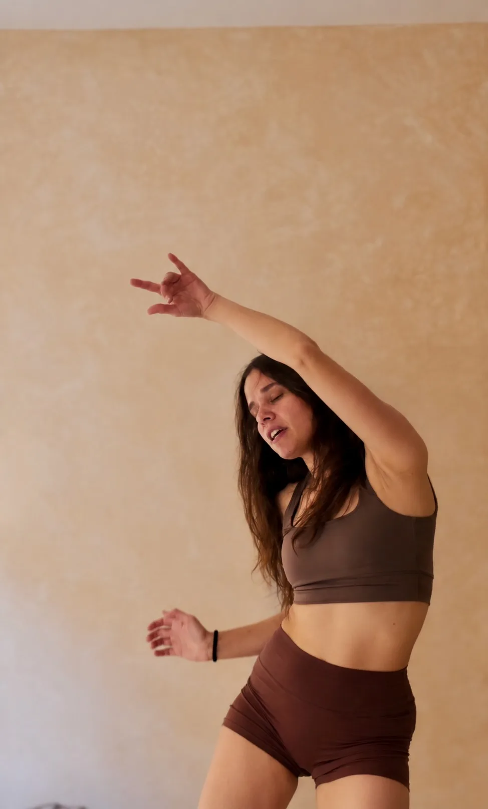Giulia dancing with one arm raised overhead, eyes closed, in a warm sunlit studio.