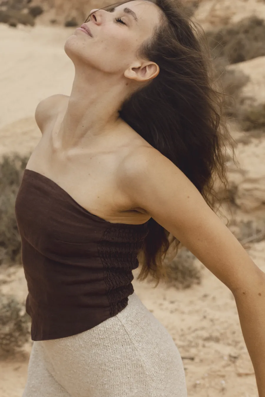 Giulia in the dunes with her eyes closed, head tilted back and arms open.
