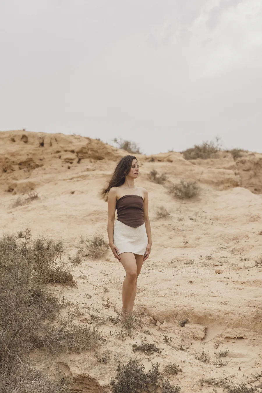 Giulia standing on a sandy hillside among dry shrubs, looking out to the side.