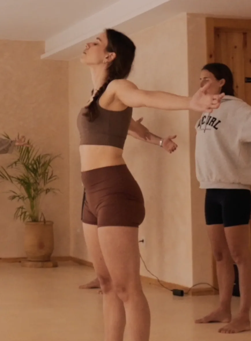 Giulia mid-practice in a sunlit studio, eyes closed, arms opening wide.