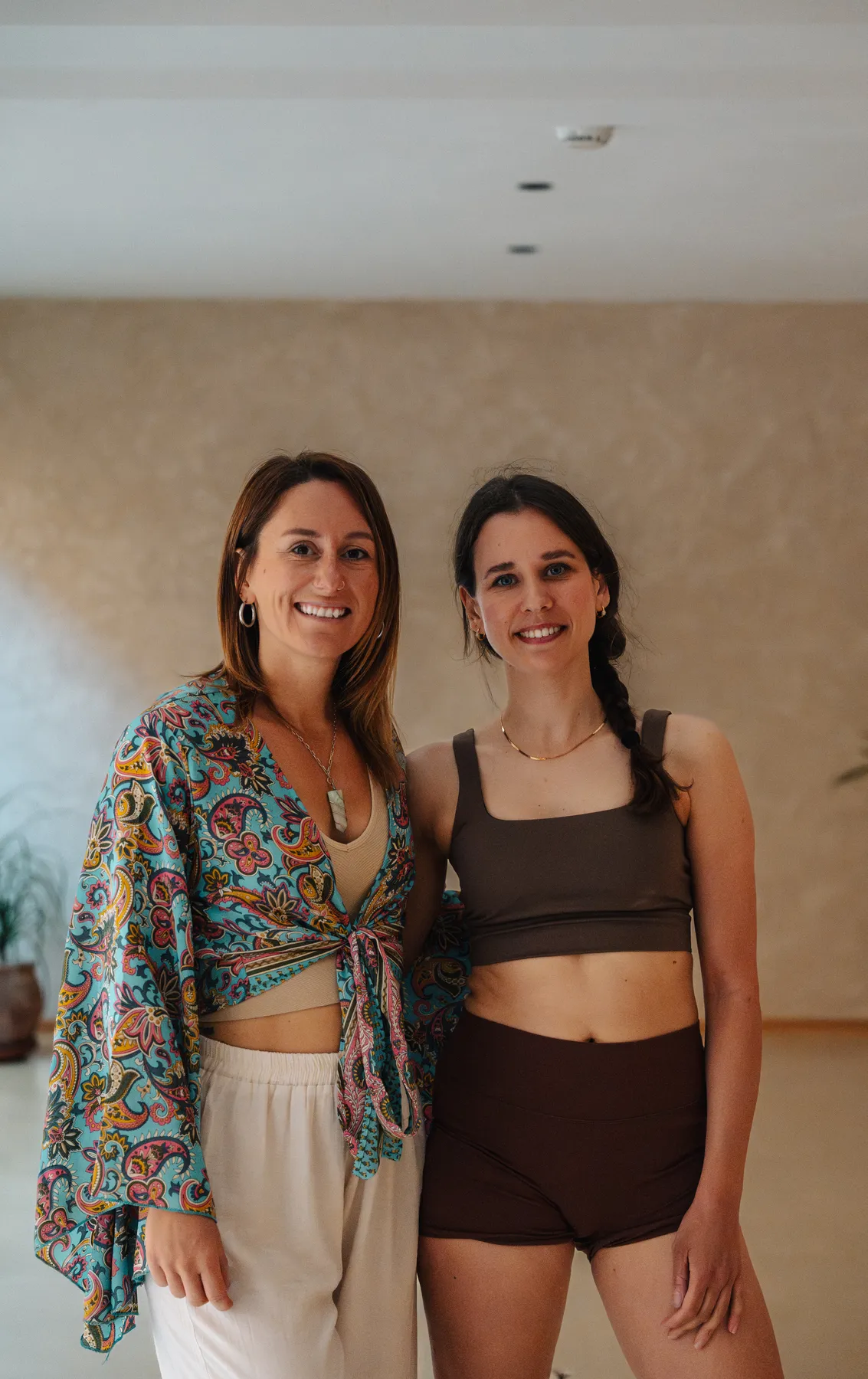 Giulia and Vanessa standing side by side in a sunlit studio, smiling.